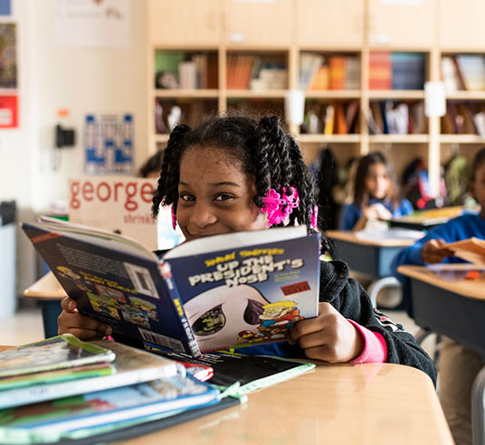 young student in classroom reading and smiling