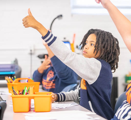 students in classroom raising hands