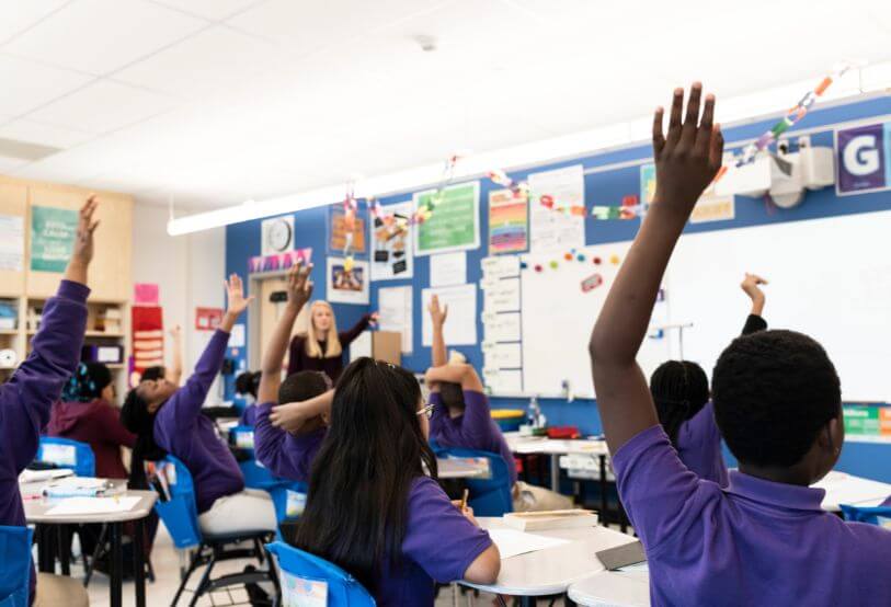 students in classroom with hands raised